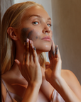Femme appliquant le gommage charbon sur sa joue, Exfoliant Noir Marc Inbane